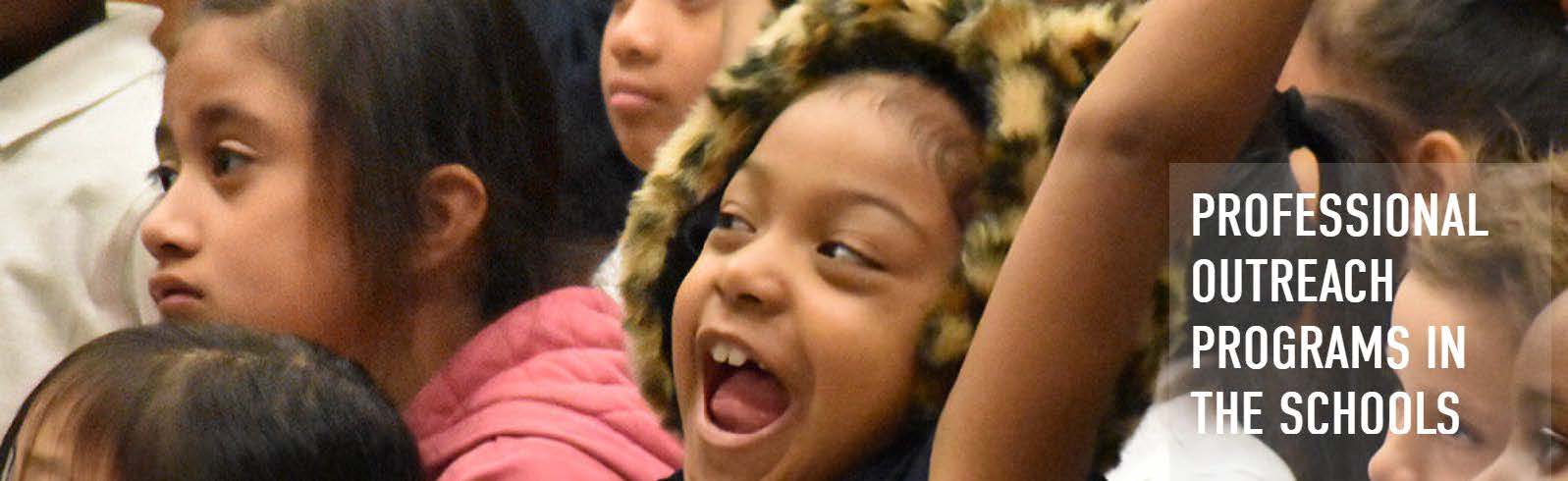 Children excitedly watching a performance. The text Professional Outreach Programs in the Schools.